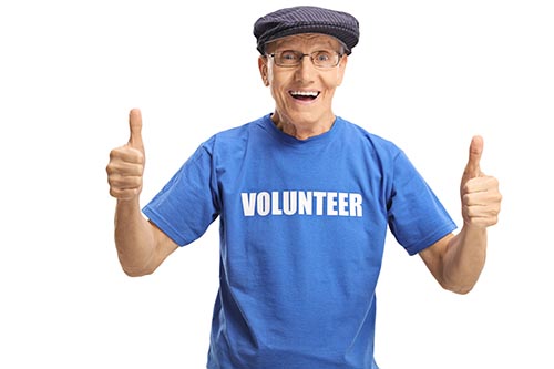 Cheerful elderly male volunteer in a blue t-shirt showing thumbs Cheerful elderly male volunteer in a blue t-shirt showing thumbs
